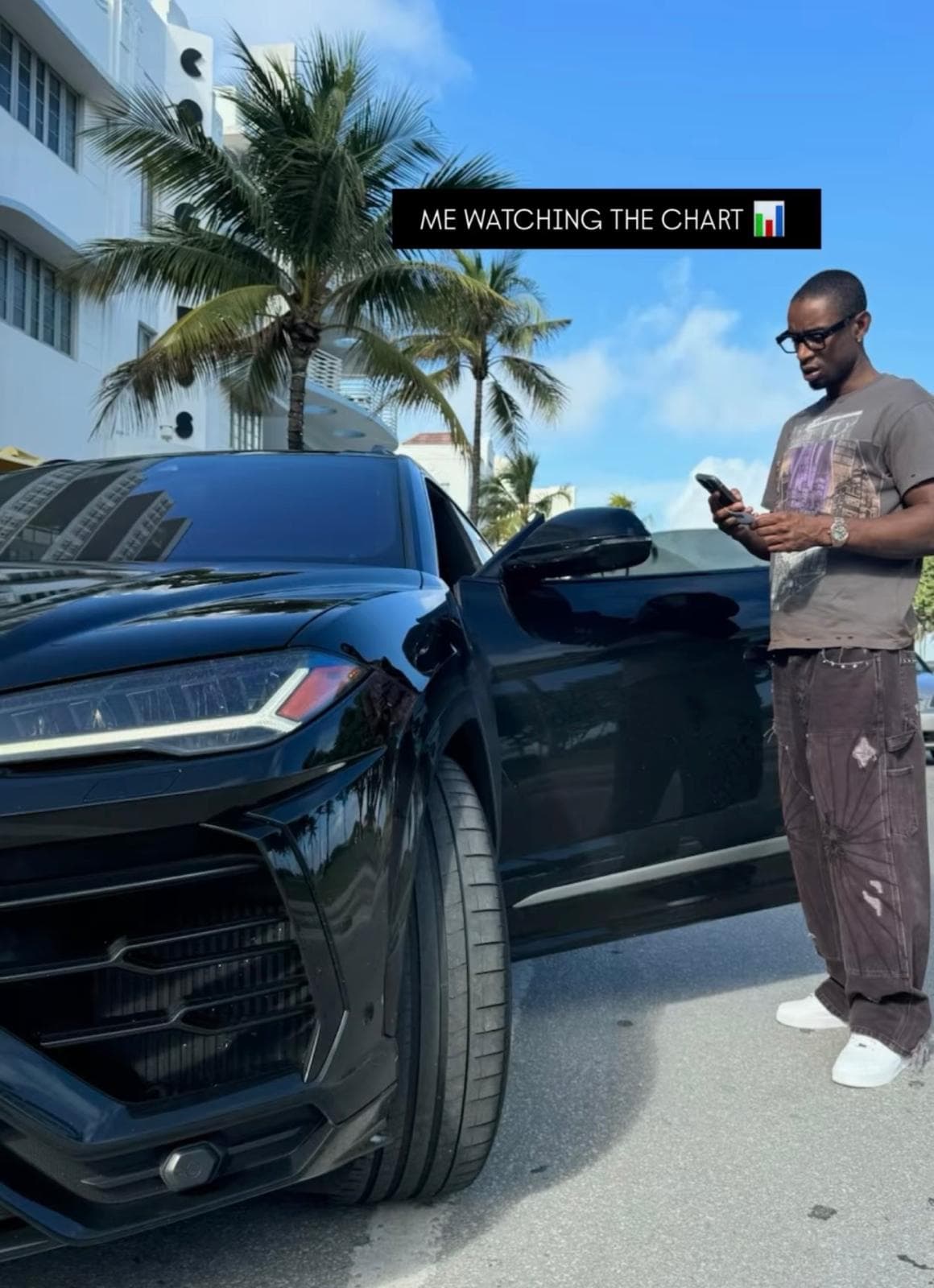 Premo watching the market beside a black car under palm trees